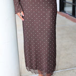 A smiling blonde woman wearing the Amara brown long-sleeve V-neck top with white polka dots by Z Supply and a tie-front detail, paired with a matching brown mesh midi Eda polka-dot skirt at Rodeo Boutique.