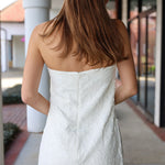Woman wearing a white strapless dress on a sidewalk.