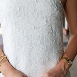 Close-up of a person wearing a white strapless dress with textured fabric, hands adjusting the hem.