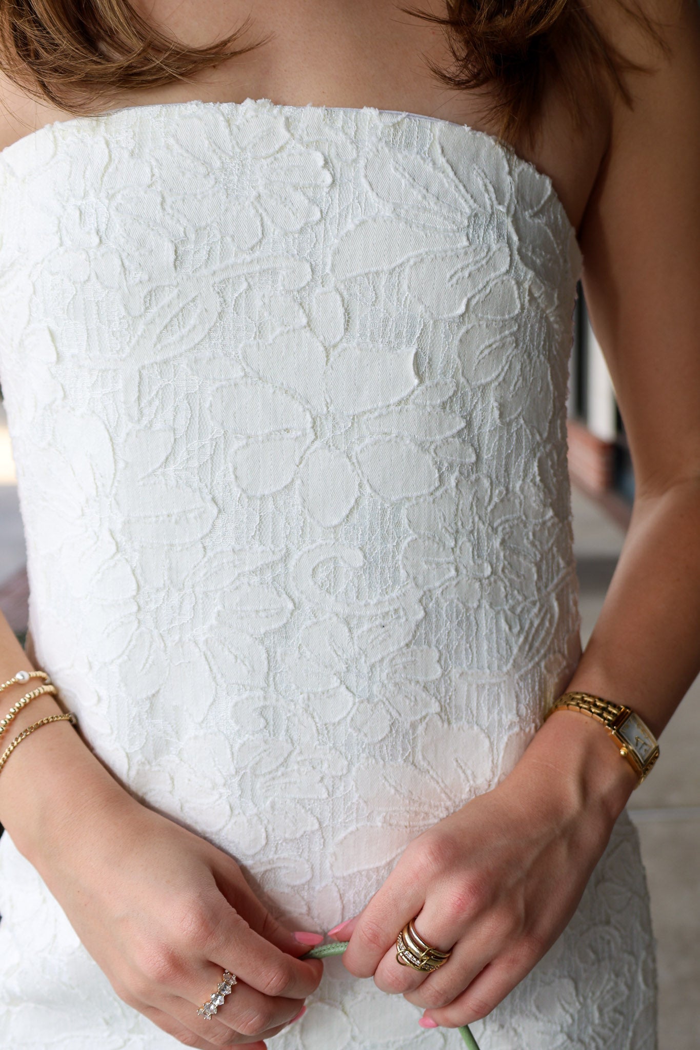 Close-up of a person wearing a white strapless dress with textured fabric, hands adjusting the hem.
