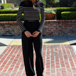 Woman wearing a black and white striped sweater and black pants standing on a brick patio.