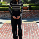 Woman wearing a black and white striped sweater and black pants standing on a brick patio.