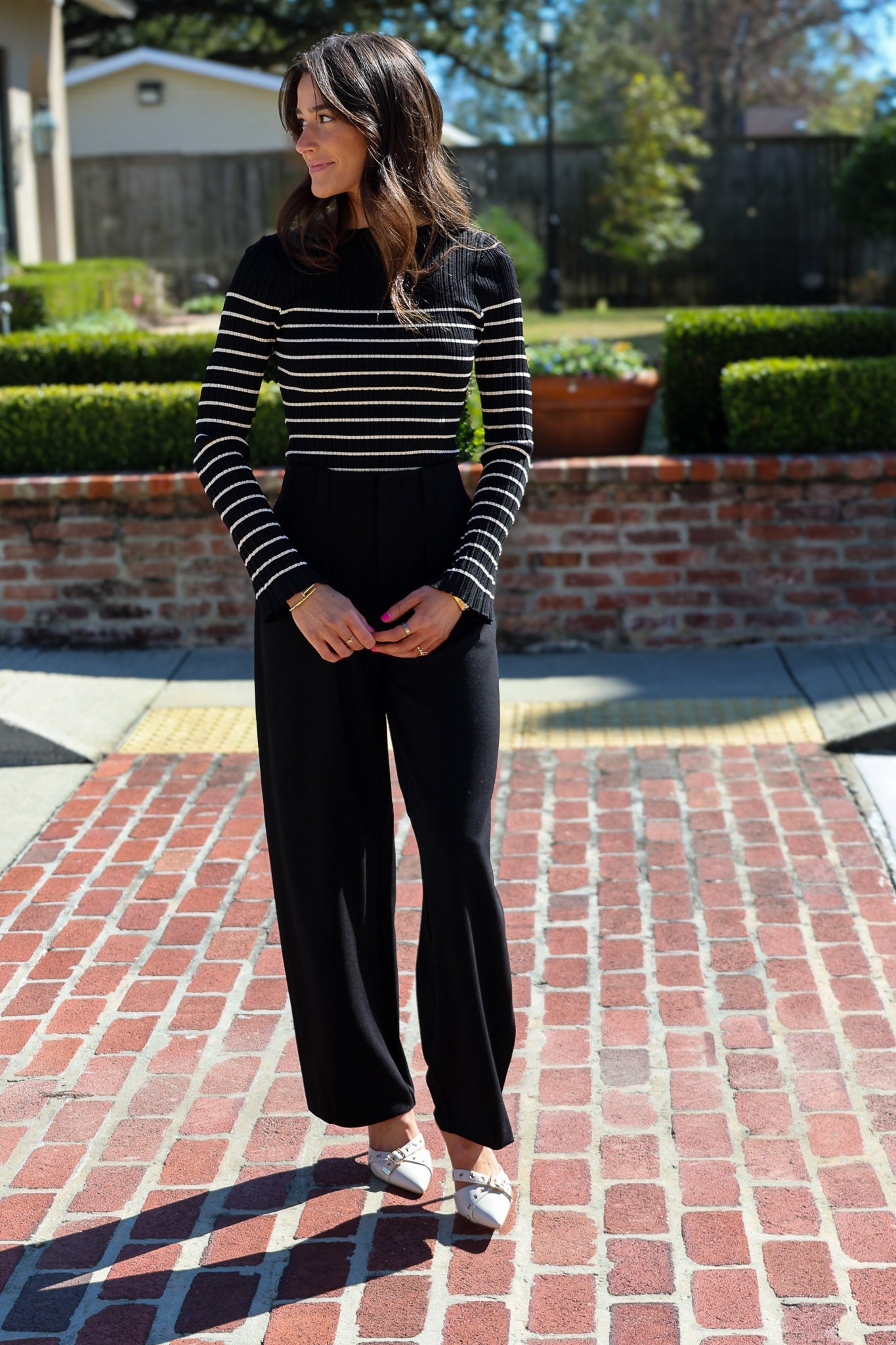 Woman wearing a black and white striped sweater and black pants standing on a brick patio.