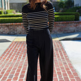 Woman wearing a black and white striped sweater and black pants on a brick driveway.