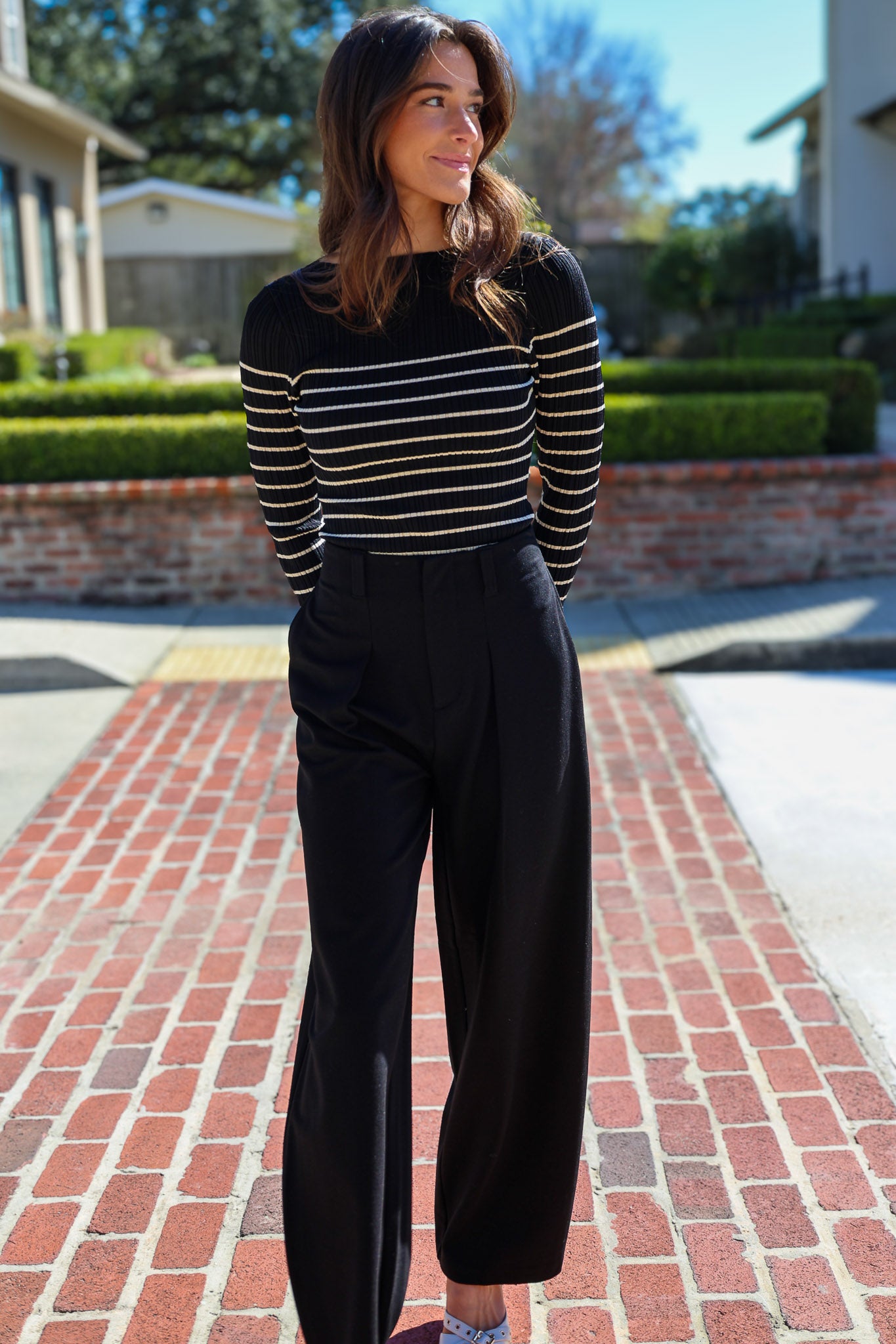 Woman wearing a black and white striped sweater and black pants on a brick driveway.