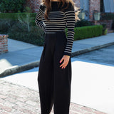 Woman wearing a striped sweater and black pants standing on a brick path with a building in the background.