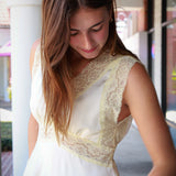 sleeveless cream-colored blouse with wide lace trim and a peplum hem, paired with blue jeans, standing in an outdoor walkway.