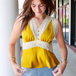 A woman wearing a sleeveless yellow top with wide lace trim and a blue denim mini skirt, standing in a covered walkway.