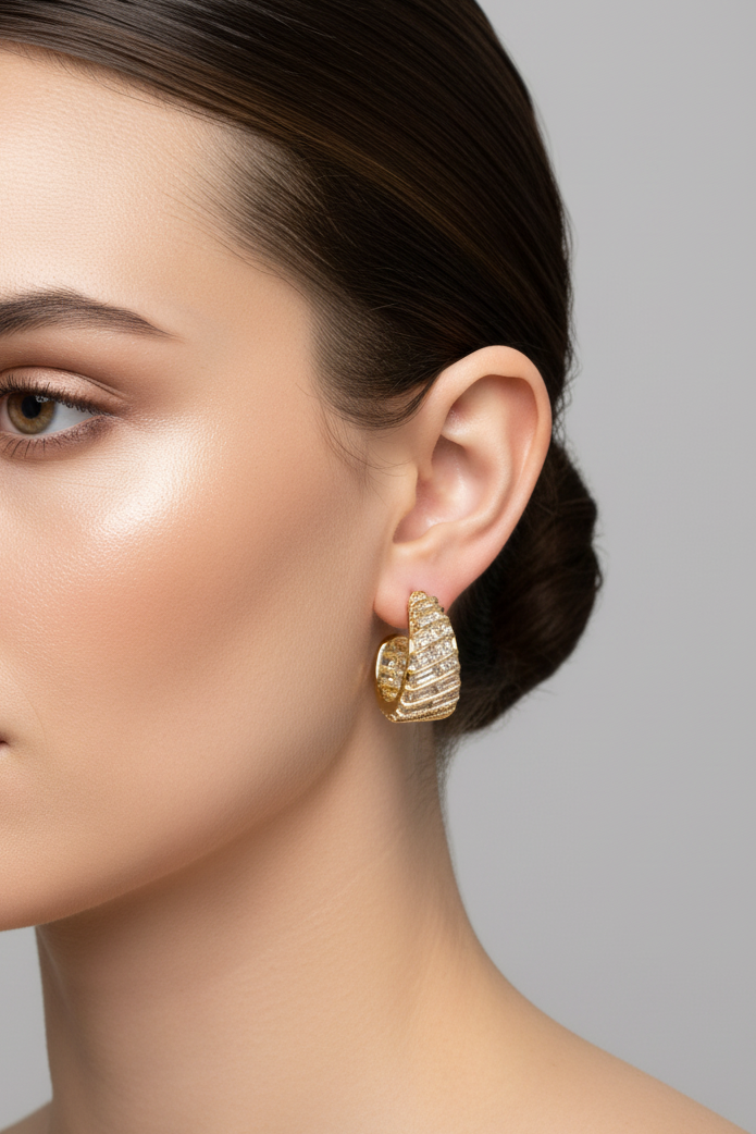 Gold huggie hoop earrings with textured horizontal ridges and small clear stones, displayed on a pink card labeled 'Rodéo BOUTIQUE'.