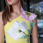 Woman wearing a yellow dress with floral embroidery, standing outdoors.