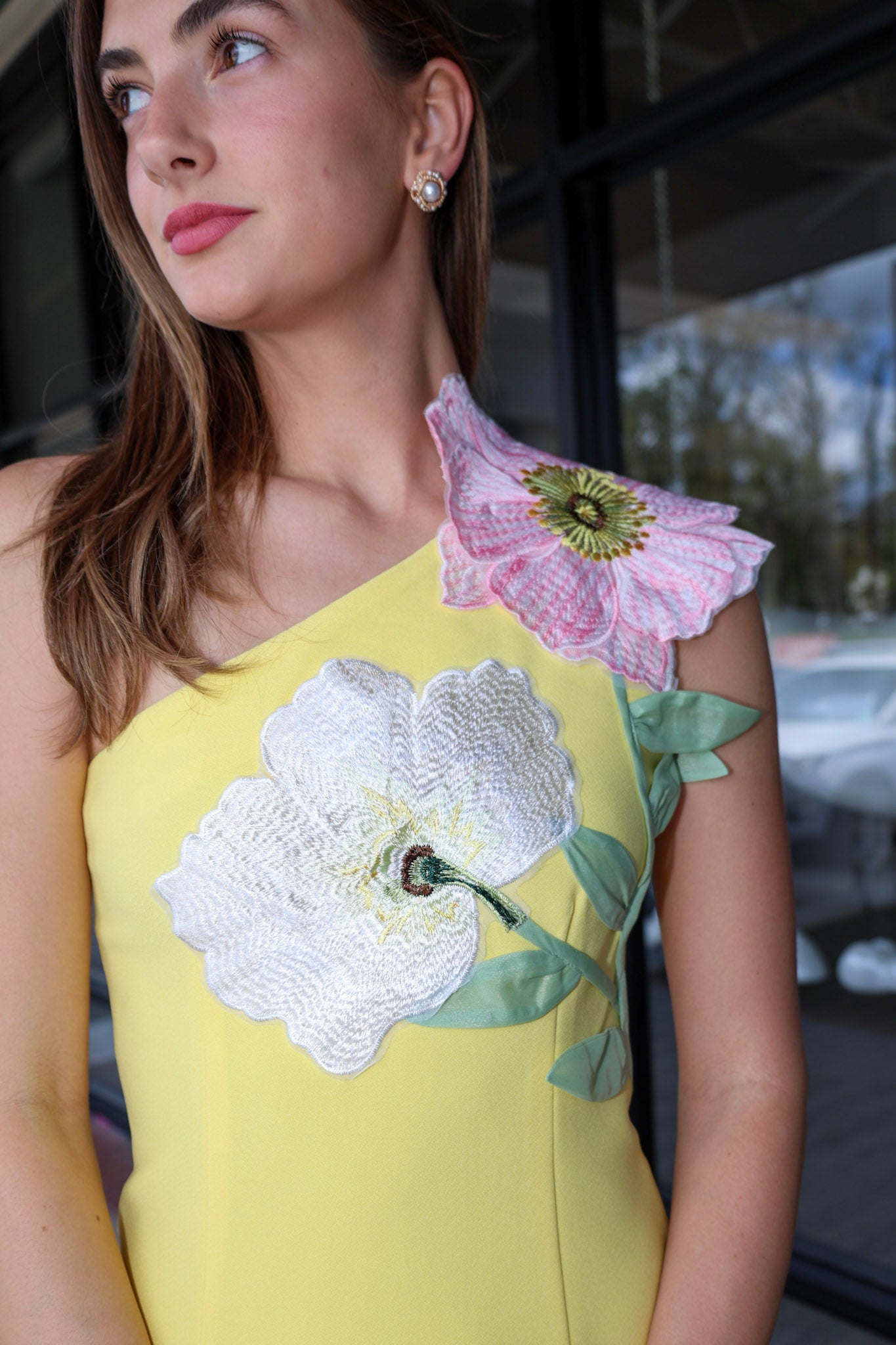 Woman wearing a yellow dress with floral embroidery, standing outdoors.