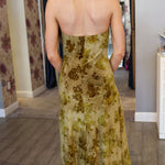 Woman wearing a floral velvet dress in a room with patterned wallpaper.