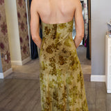 Woman wearing a floral velvet dress in a room with patterned wallpaper.