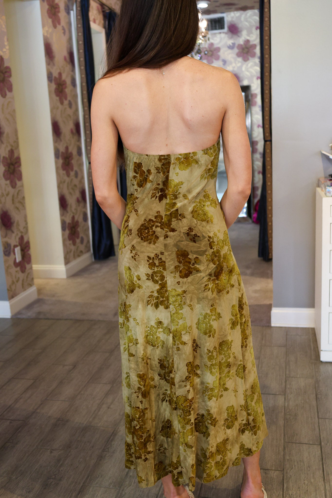 Woman wearing a floral velvet dress in a room with patterned wallpaper.
