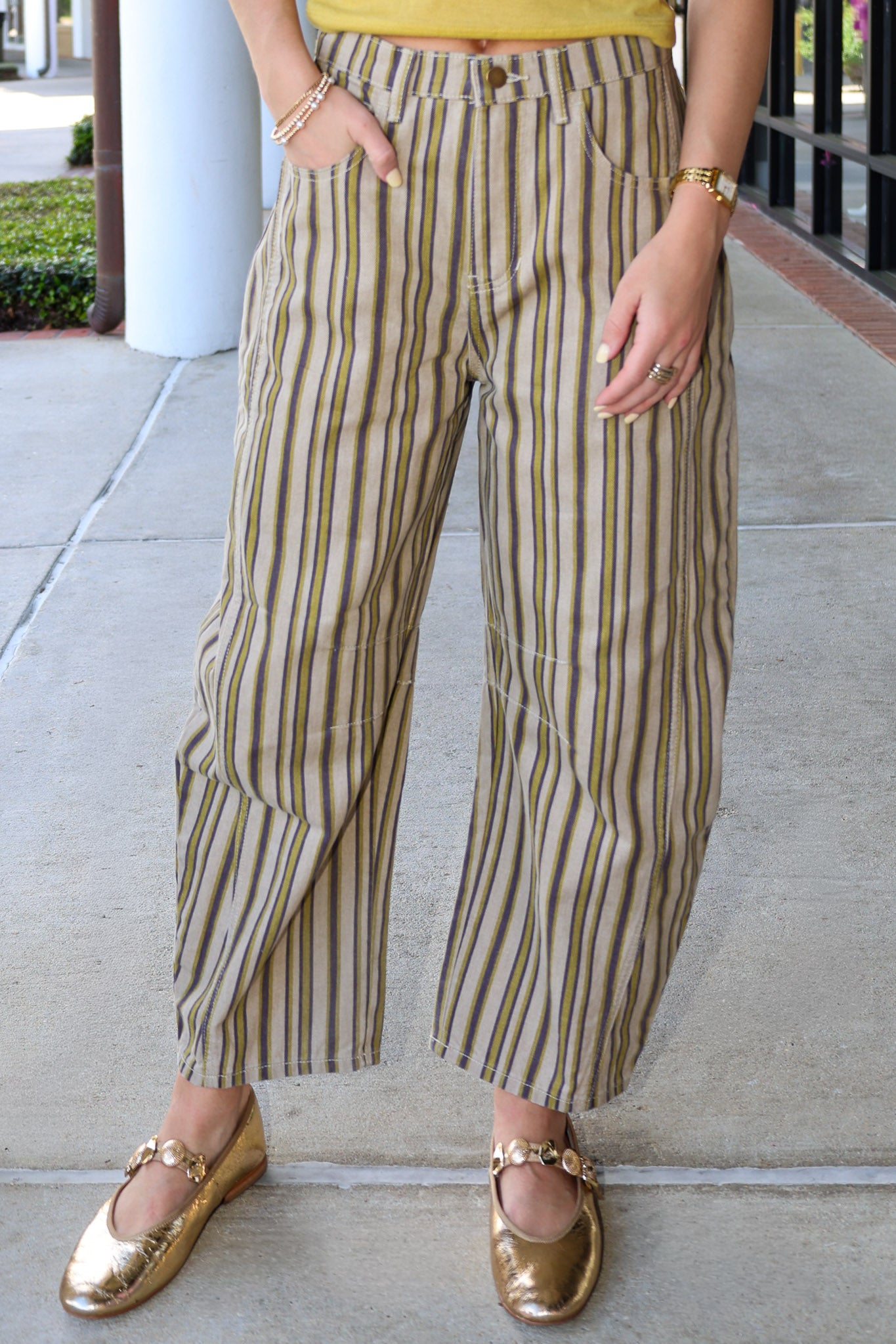 Person wearing striped pants and gold shoes on a sidewalk.
