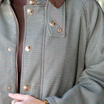 Close-up of a person wearing a small-scale houndstooth pattern jacket in gray and brown, featuring a solid brown corduroy collar and gold-tone metal buttons.