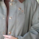 Close-up of a person wearing a small-scale houndstooth pattern jacket in gray and brown, featuring a solid brown corduroy collar and gold-tone metal buttons.