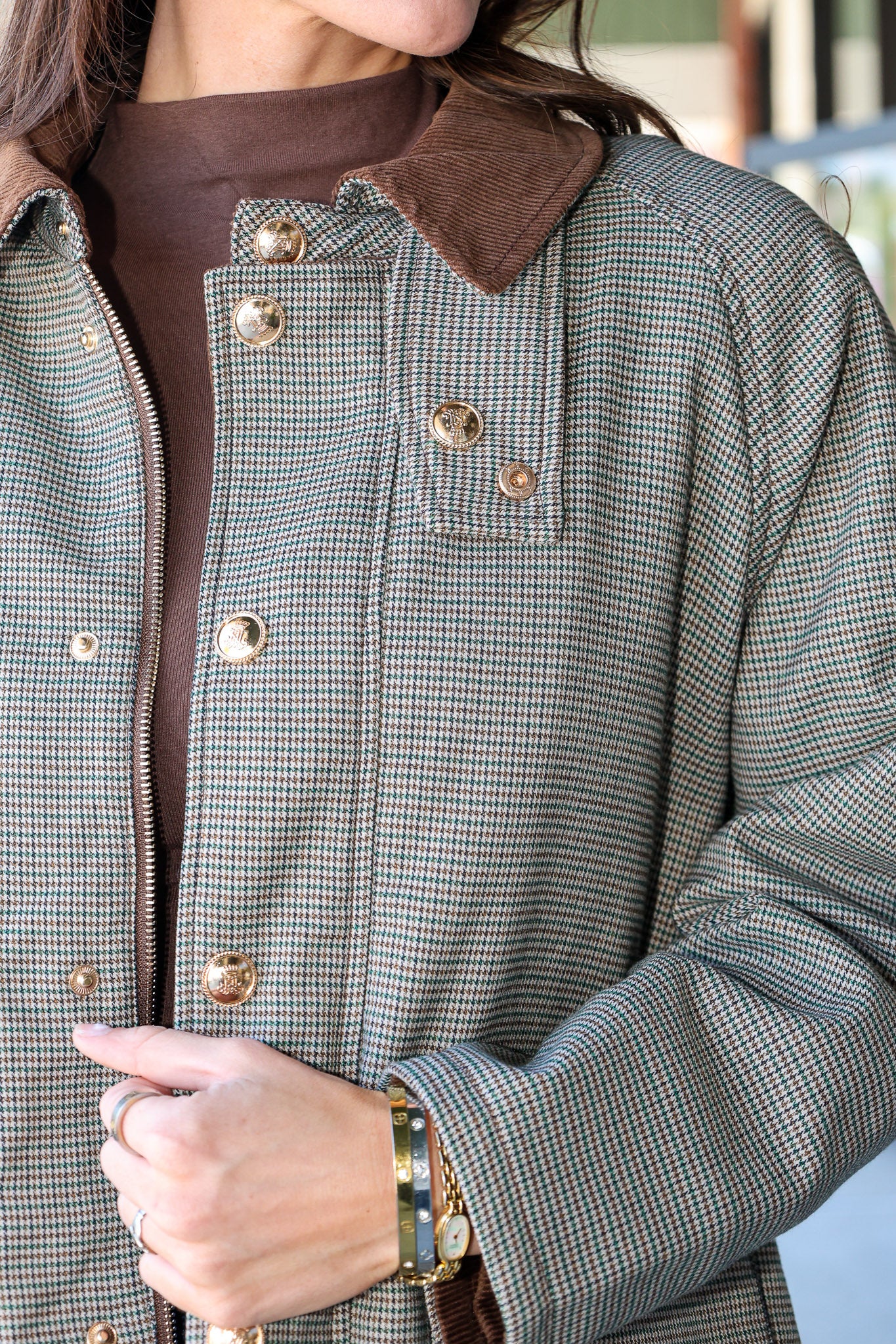 Close-up of a person wearing a small-scale houndstooth pattern jacket in gray and brown, featuring a solid brown corduroy collar and gold-tone metal buttons.