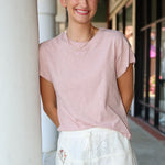 Woman wearing a pink top and white shorts with floral embroidery, standing against a building exterior.