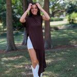A woman tailgating at LSU  wearing a dark brown high-low cape top, a white mini skirt, and white cowboy boots.