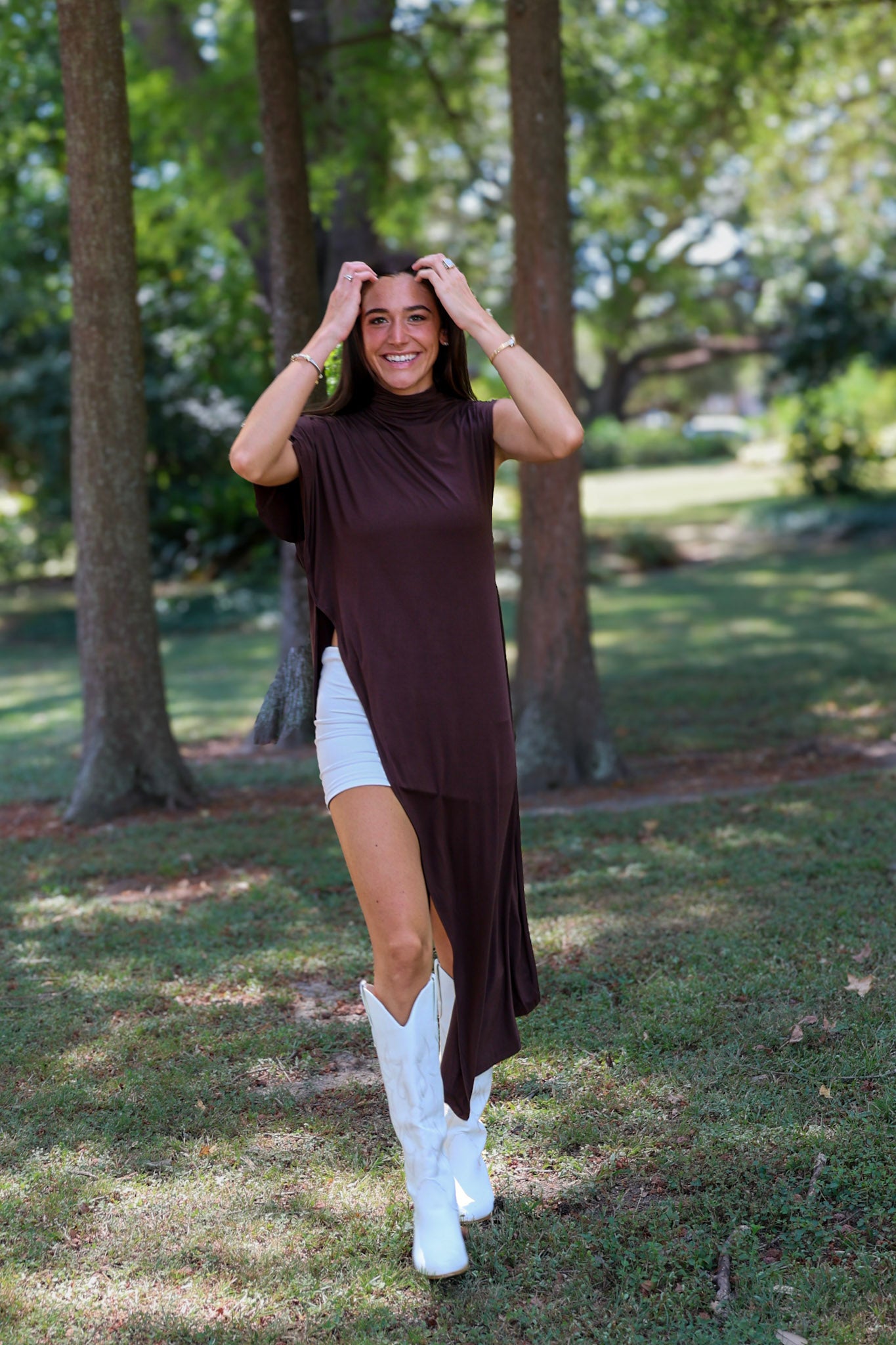 A woman tailgating at LSU  wearing a dark brown high-low cape top, a white mini skirt, and white cowboy boots.