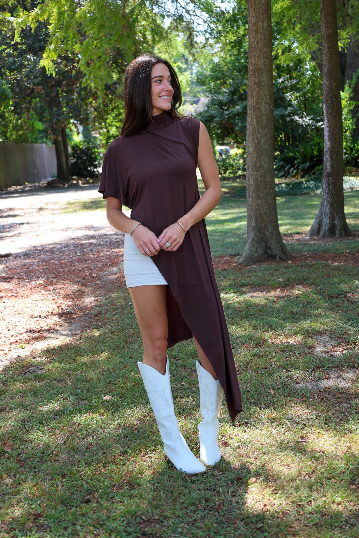 A woman tailgating at LSU  wearing a dark brown high-low cape top, a white mini skirt, and white cowboy boots.