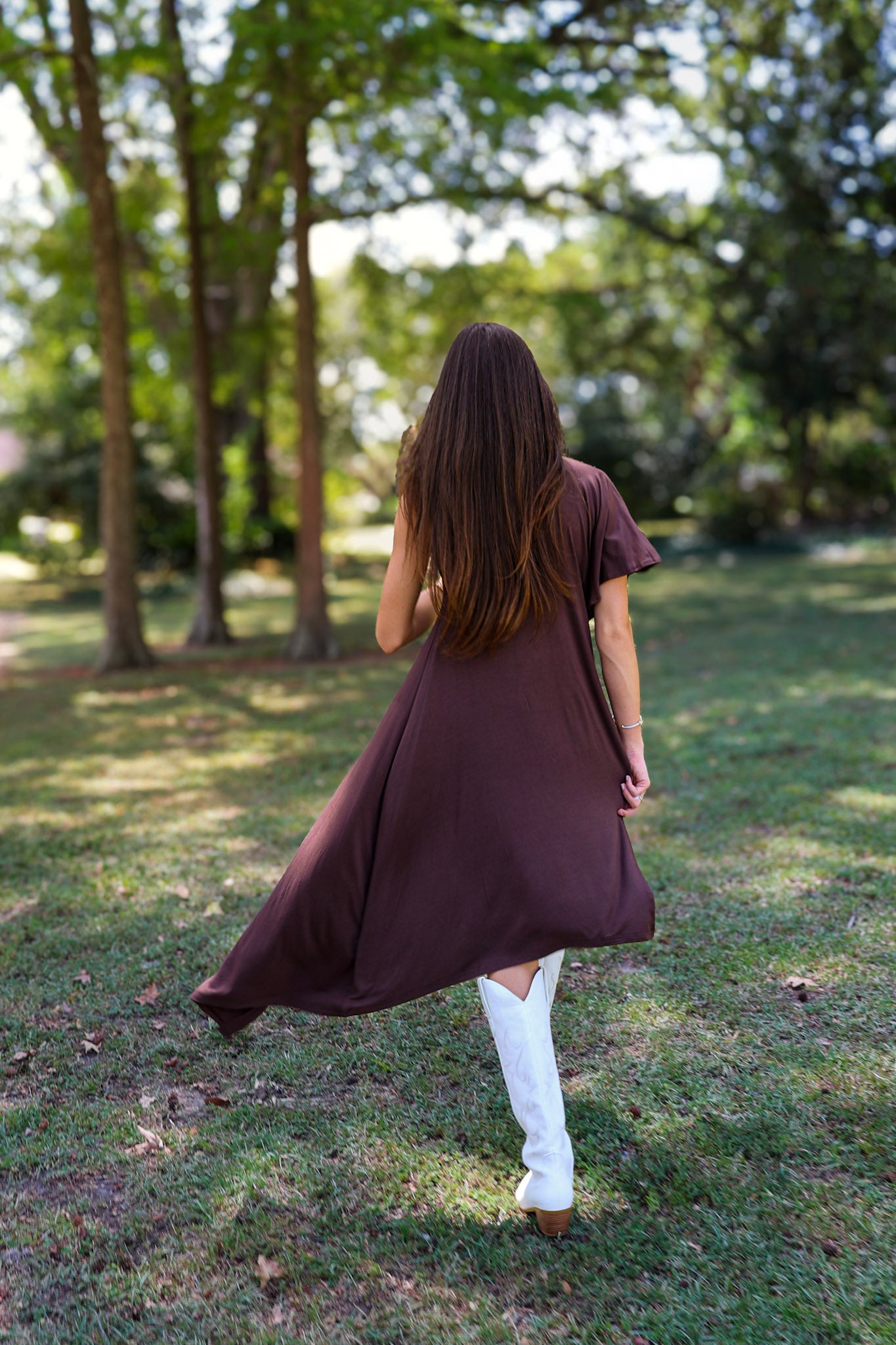 A woman tailgating at LSU  wearing a dark brown high-low cape top, a white mini skirt, and white cowboy boots.