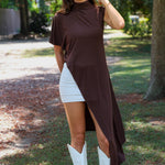 A woman tailgating wearing a dark brown high-low cape top, a white mini skirt, and white cowboy boots.