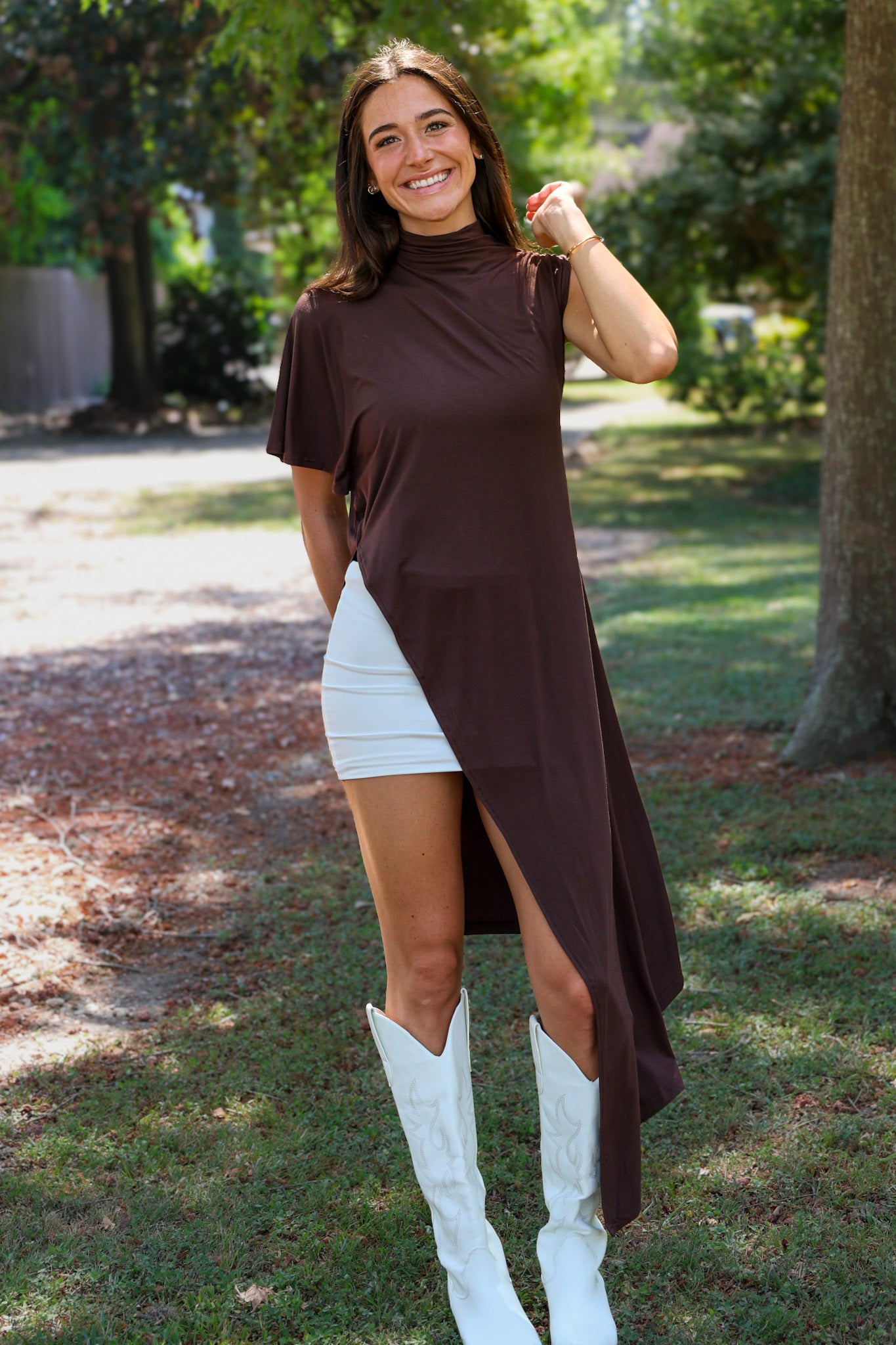 A woman tailgating wearing a dark brown high-low cape top, a white mini skirt, and white cowboy boots.