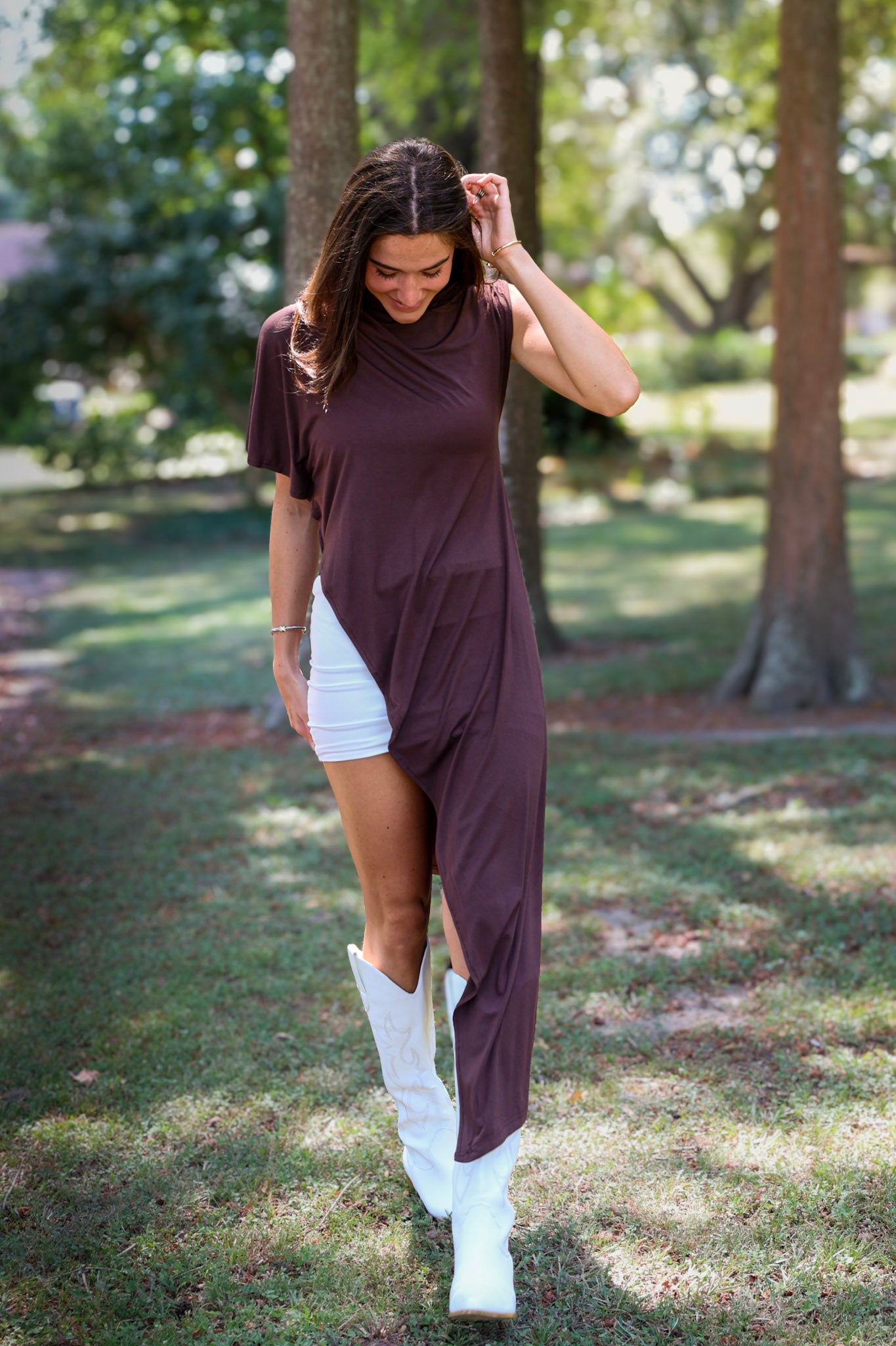 A woman tailgating at LSU  wearing a dark brown high-low cape top, a white mini skirt, and white cowboy boots.