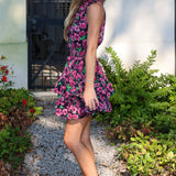 Woman in a floral dress standing outdoors on a gravel path with greenery.