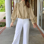 Woman wearing a khaki jacket and white pants standing outdoors.