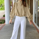 Woman wearing a khaki jacket and white pants standing outdoors.