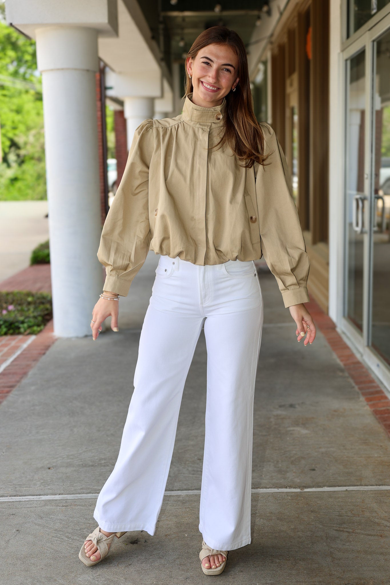 Woman wearing a khaki jacket and white pants standing outdoors.