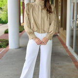 Woman wearing a khaki jacket and white pants standing outdoors.