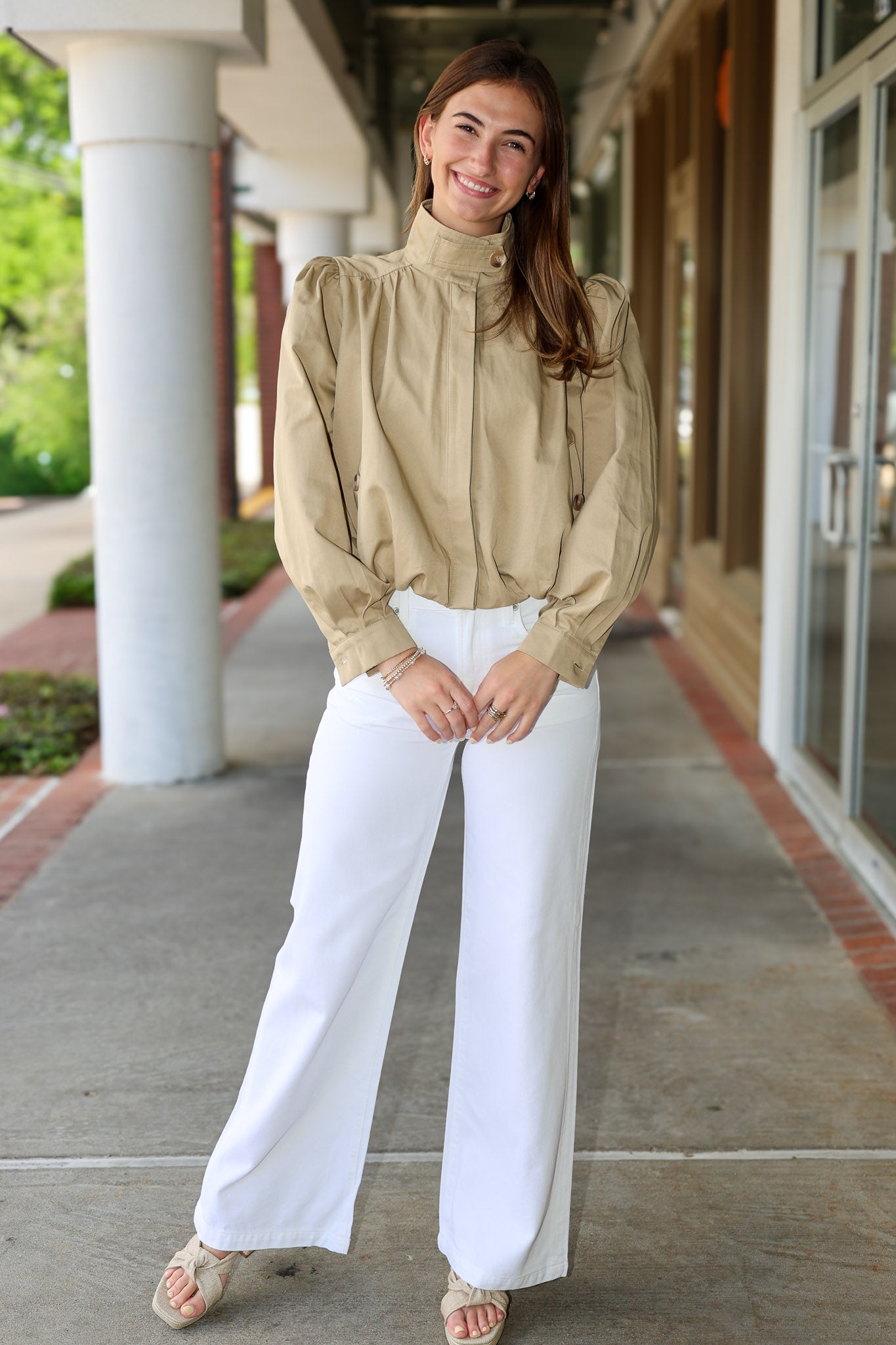 Woman wearing a khaki jacket and white pants standing outdoors.