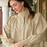 Woman wearing a khaki jacket and white pants standing outdoors.
