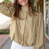 Woman wearing a khaki jacket and white pants standing outdoors.
