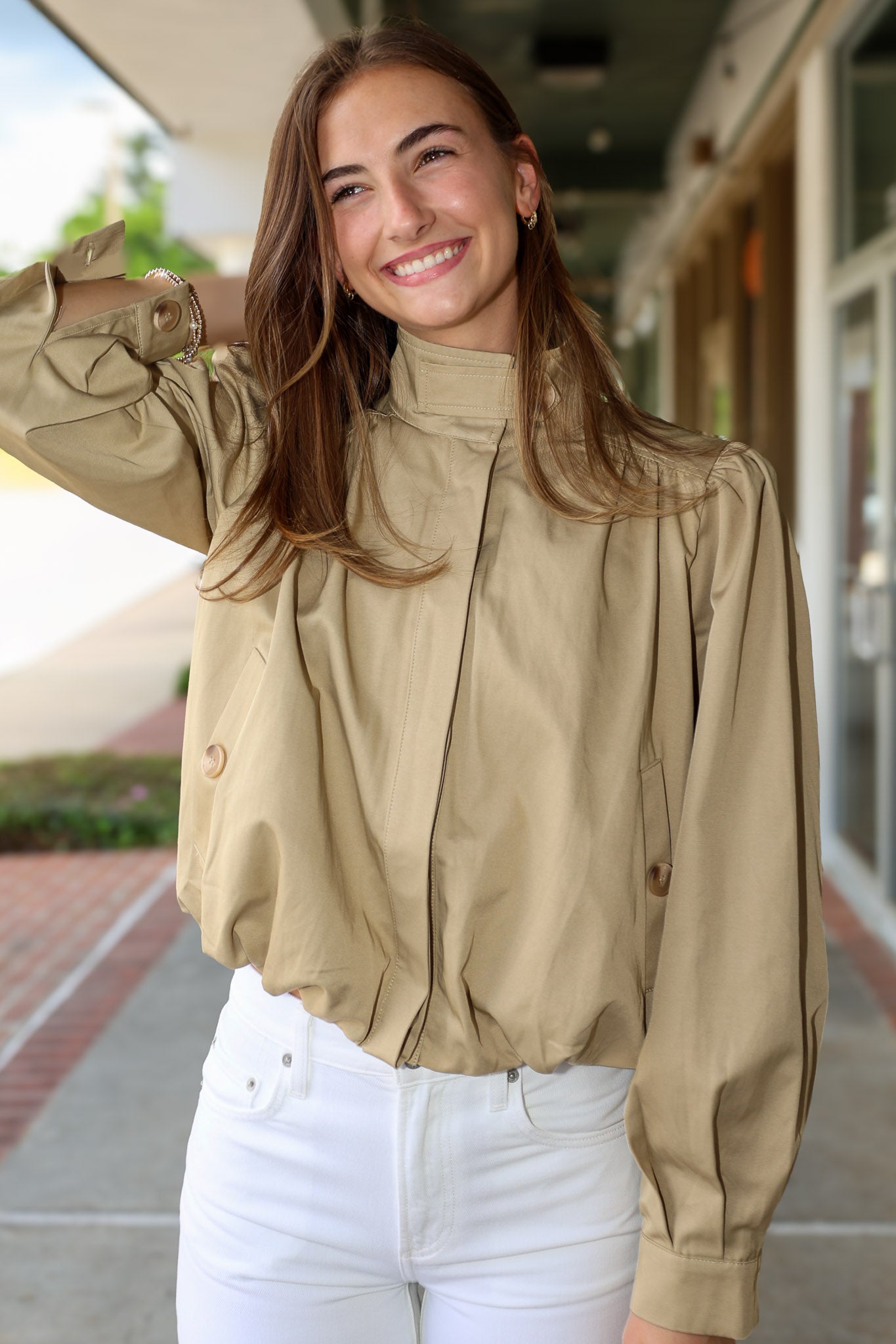 Woman wearing a khaki jacket and white pants standing outdoors.
