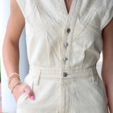 Person wearing a cream-colored sleeveless dress with buttons.