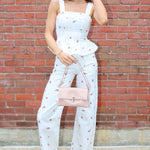 Woman in a light blue floral dress standing against a brick wall.