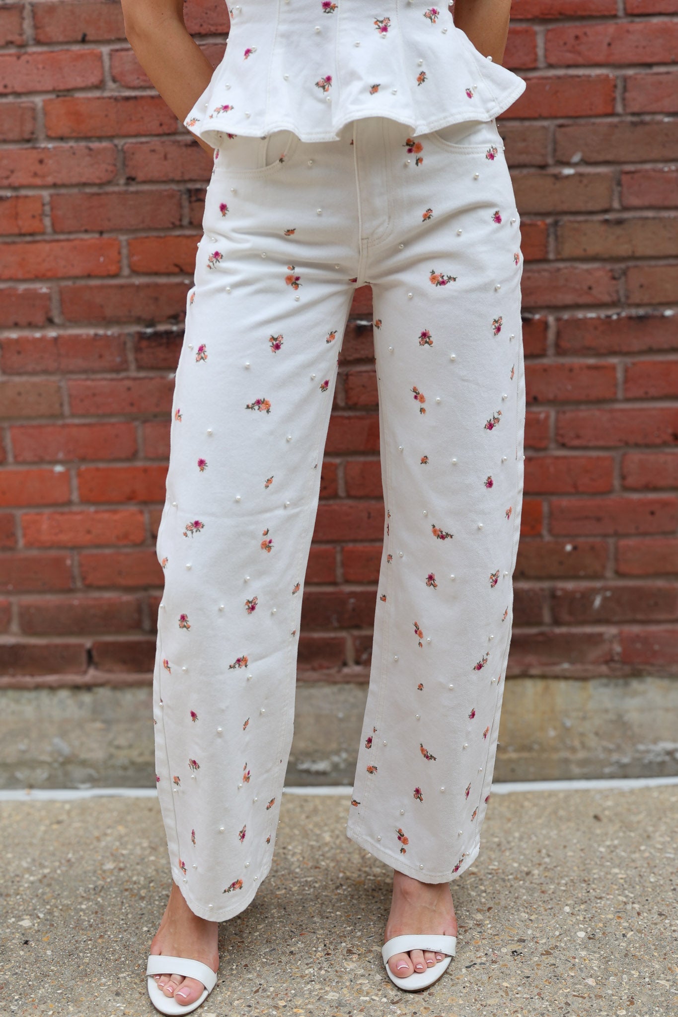 Person wearing a white outfit with floral patterns against a brick wall.