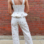 Woman wearing a white jumpsuit with a ruffled top against a brick wall.