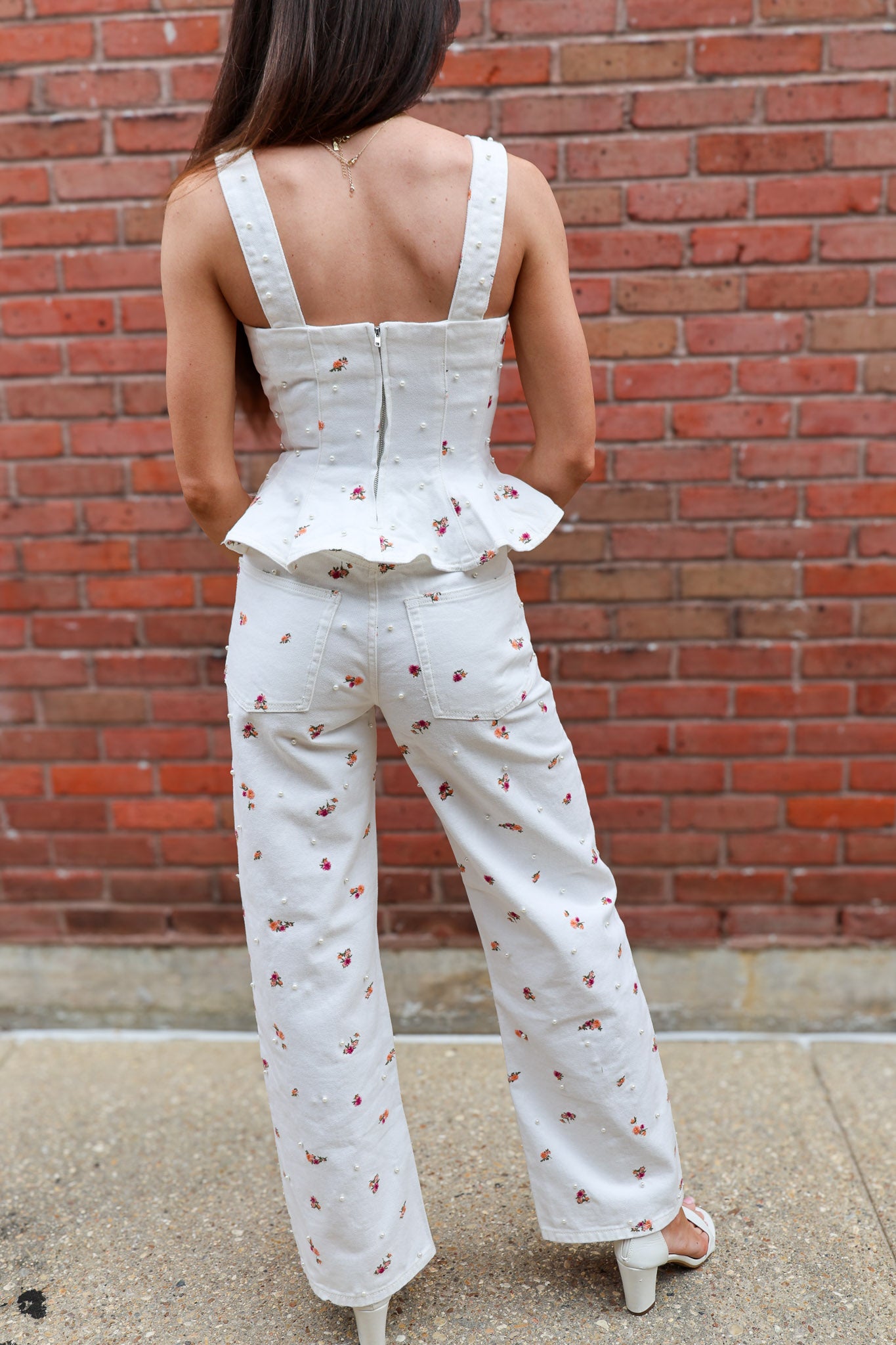 Woman wearing a white jumpsuit with a ruffled top against a brick wall.