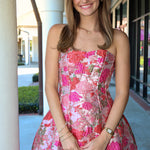 Woman wearing a strapless pink tones floral dress standing outdoors.