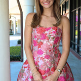 Woman wearing a strapless pink tones floral dress standing outdoors.