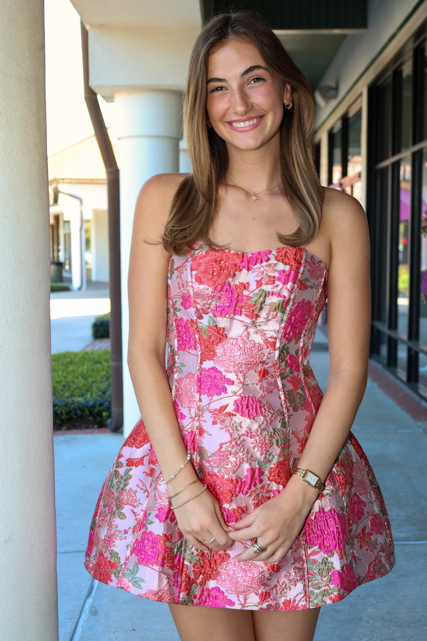 Woman wearing a strapless pink tones floral dress standing outdoors.