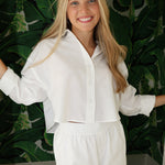 Woman wearing a white outfit standing against a green leafy background