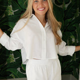 Woman wearing a white outfit standing against a green leafy background