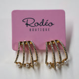 Pair of gold and pearl earrings on a pink card with 'Rodeo Boutique' branding.